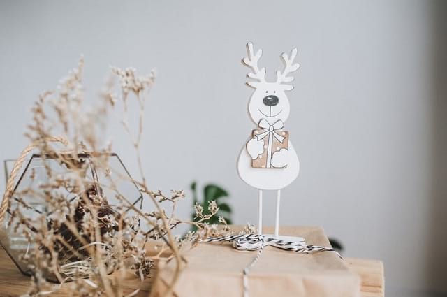 ¿Por qué crear una lista de deseos para estos días festivos? A brown paper package with a polar bear reindeer cut out standing on it with some fake Christmas branches on the left.